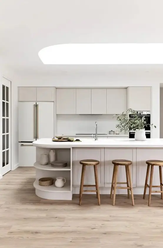 a chic neutral kitchen with shaker style cabinets, a curved kitchen island with open storage compartments and a skylight over it