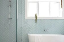 a contemporary bathroom with dusty blue herringbone tiles, an oval tub, a shower, a basket and a stool is welcoming