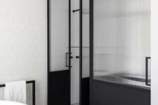 a contemporary bathroom with white hex tiles and granite floors, a white oval tub, a black metal and fluted glass space divider