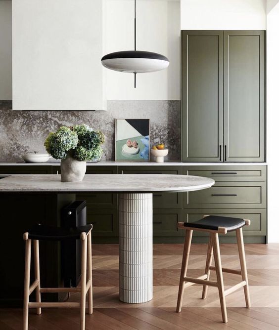a contemporary kitchen with dark green shaker cabinets, a kitchen island with a curved countertop, black stools and lamps