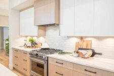 a contemporary kitchen with flat panel stained and white cabinets, a white backsplash and white countertops and black fixtures