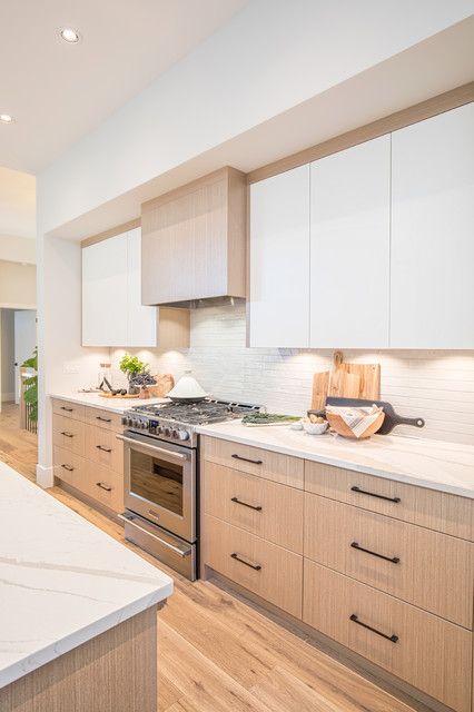 a contemporary kitchen with flat panel stained and white cabinets, a white backsplash and white countertops and black fixtures