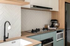 a contemporary kitchen with sage green and white flat panel cabinets, wooden countertops, a white herringbone tile backsplash