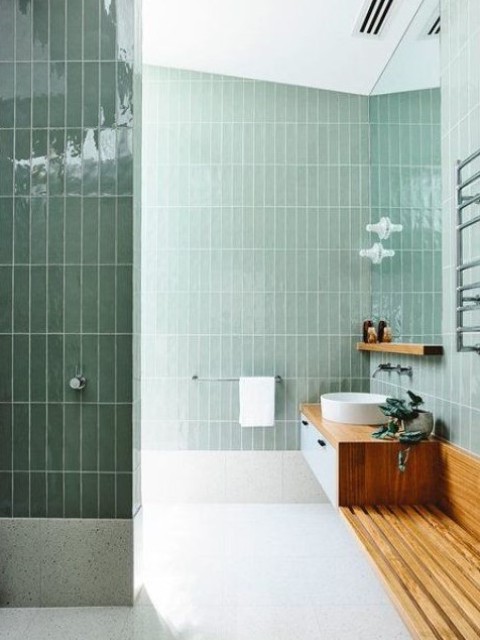 a contemporary light green bathroom clad with tiles, a floating wooden vanity and a round sink is chic