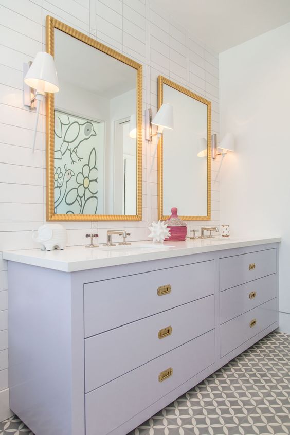 a cool bathroom in neutrals with skinny and printed tiles, a lilac double vanity, mirrors in gold frames and wall sconces