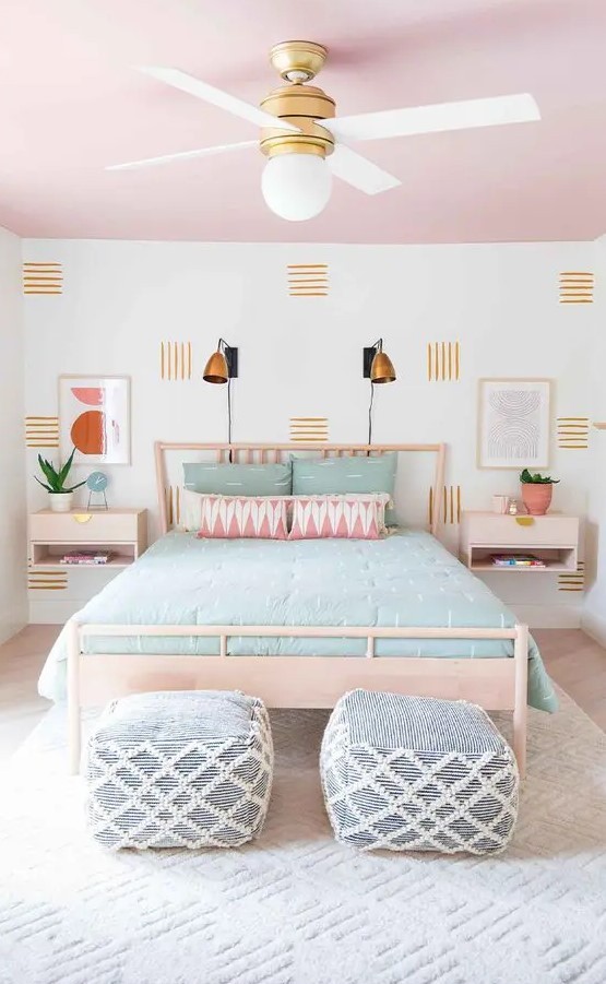 a cool pastel bedroom with a pink ceiling, a light-stained bed and nightstands, pastel bedding, blue and white poufs