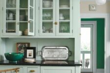 a cozy mint green kitchen with glass front and shaker style cabinets, black countertops and a mint backsplash, stained furniture