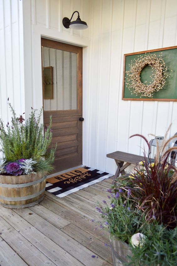 a cozy rustic entrance with a stained Dutch door, layered rugs, a bench, potted plants and blooms, a wreath in a frame