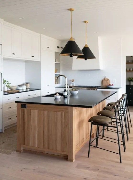 a cozy white kitchen with shaker cabinets, a stained kitchen island, black countertops, black and gold lamps and awesome stools