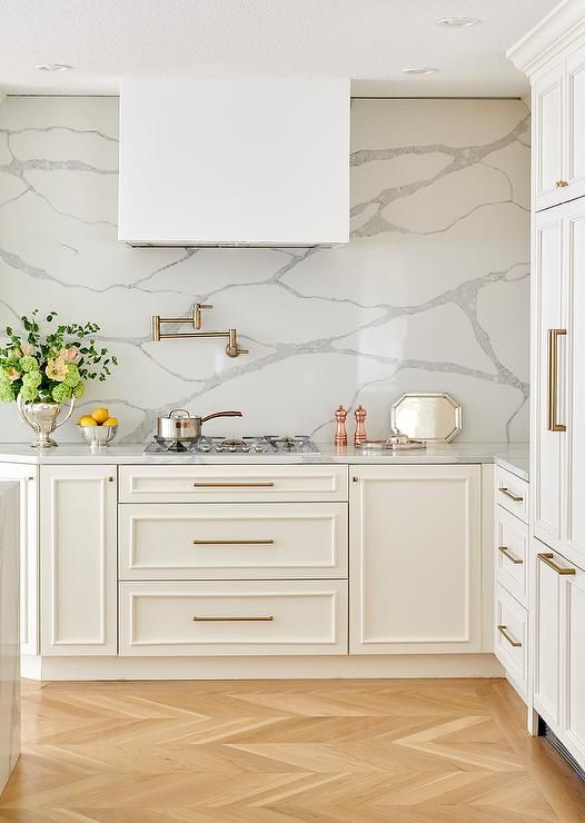 a creamy farmhouse kitchen with shaker cabinets, white quartz countertops and a backsplash, brass handles is a lovely space