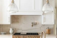 a creamy kitchen with shaker cabinets, a neutral quartz backsplash and countertops, vintage glass pendant lamps
