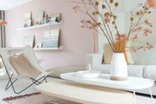 a delicate Scandinavian living room with blush walls, a neutral sofa, a neutral chair, two coffee tables and ledges