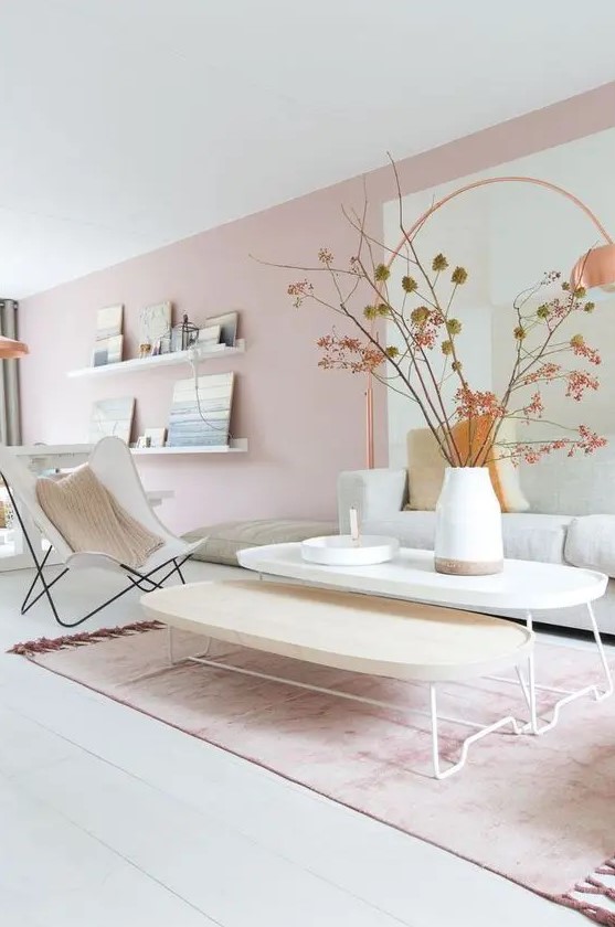 a delicate Scandinavian living room with blush walls, a neutral sofa, a neutral chair, two coffee tables and ledges