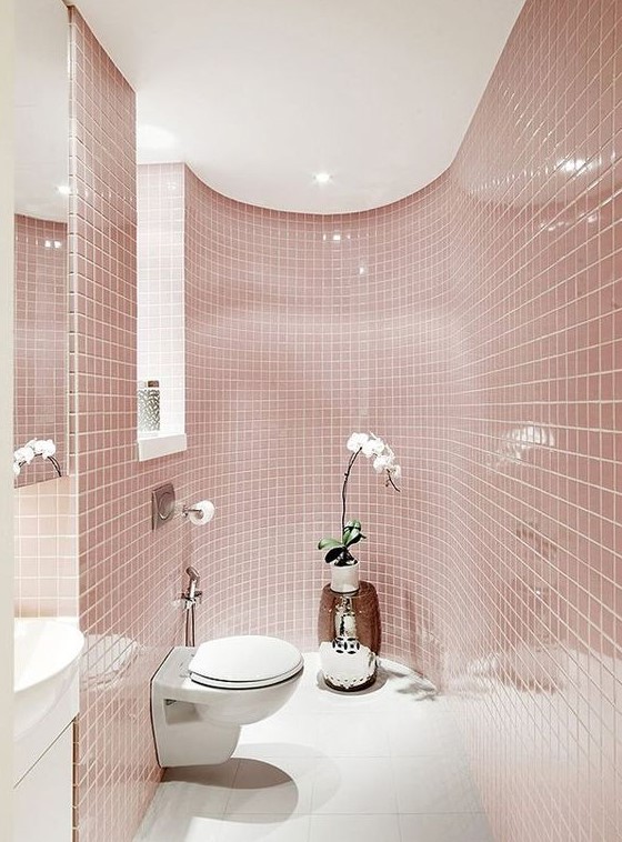 a delicate blush bathroom all clad with tiles, with a window, white appliances and a potted orchid for a touch of luxury