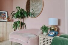 a delicate dusty pink living room with a matching chair, a green sofa, an IKEA table, a cabinet, potted plants and a round mirror