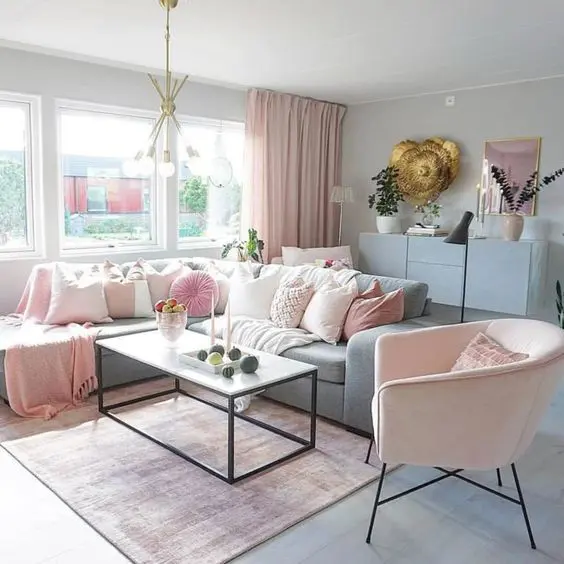 a delicate pastel living room with a dusty blue credenza, a dusty blue sofa and a chair, pink pillows, potted plants and a coffee table