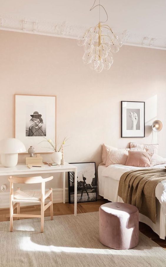 a delicate pastel pink bedroom with a bed and pink and white bedding, a lilac pouf, a white vanity, a neutral chair and a cool bubble chandelier