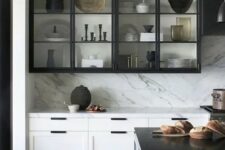 a dramatic black and white kitchen with shaker and glass cabinets, a white kitchen island with a black countertop, a white backsplash