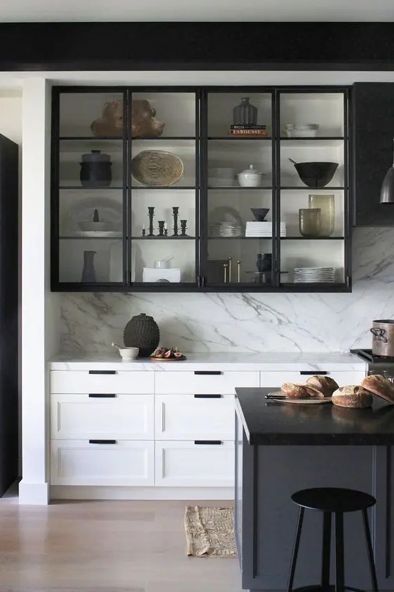 a dramatic black and white kitchen with shaker and glass cabinets, a white kitchen island with a black countertop, a white backsplash