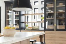 a dramatic kitchen with light-stained and black cabinets, glass front ones, a large stained kitchen island, black pendant lamps