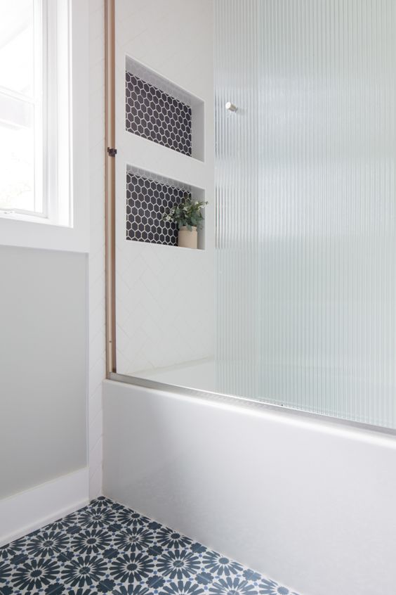 a farmhouse bathroom with niche shelves, a reeded glass shower screen and a printed tile floor is amazing