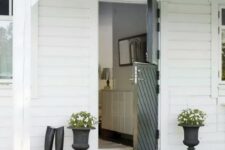 a farmhouse entrance with a black diagonal stripe Dutch door, black urns with white blooms and greenery and riding boots is very cozy and bold
