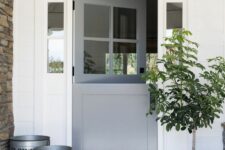 a farmhouse porch with a grey Dutch door, metal buckets with a tree, a rug is a cool space with an industrial feel