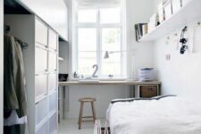 a functional white Scandinavian bedroom with a working space by the window, a bed, a wardrobe composed in a creative way