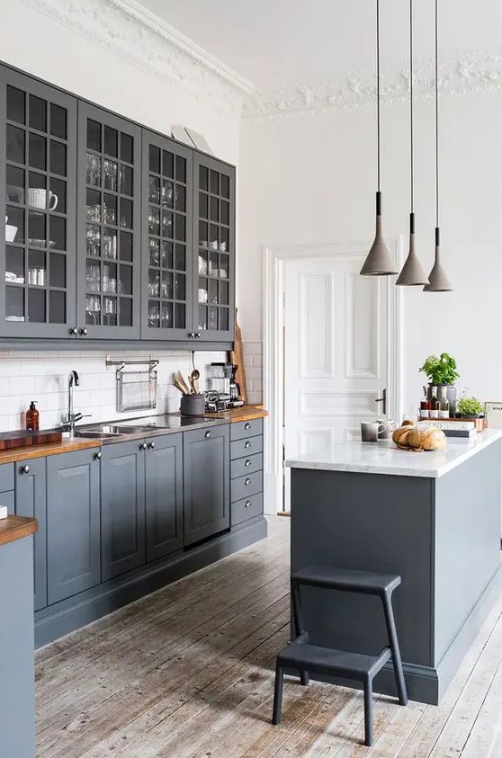 a graphite grey kitchen with shaker and glass cabinets, a white subway tile backsplash, butcherblock countertops and pendant lamps