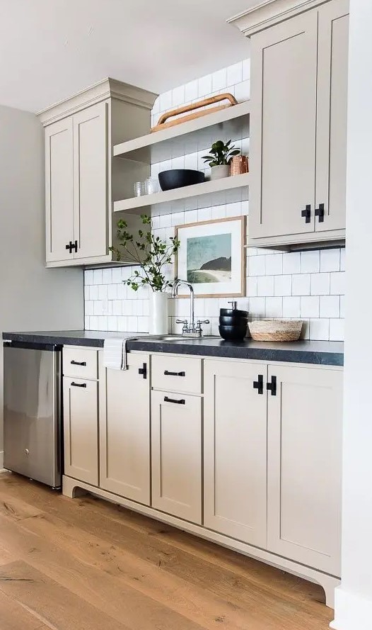a greige kitchen with a white square tile backsplash, open shelves, and black countertops is a stylish space with a farmhouse feel
