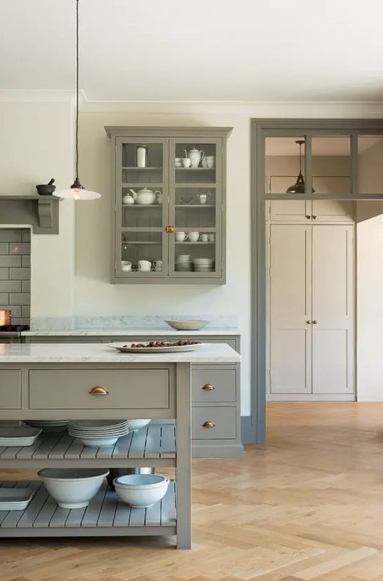 a grey kitchen with flat panel and glass cabinets, a white marble backsplash and countertops and a large kitchen island