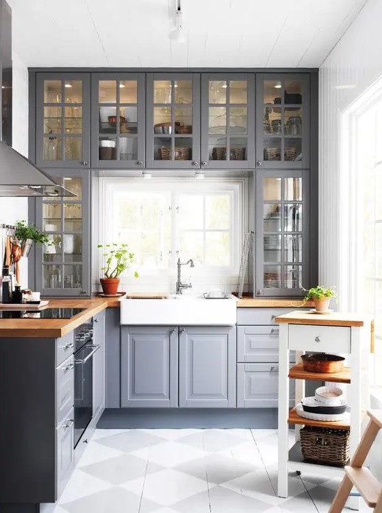 a grey kitchen with shaker and glass cabinets, butcherblock countertops, a tiny kitchen island and a window backsplash