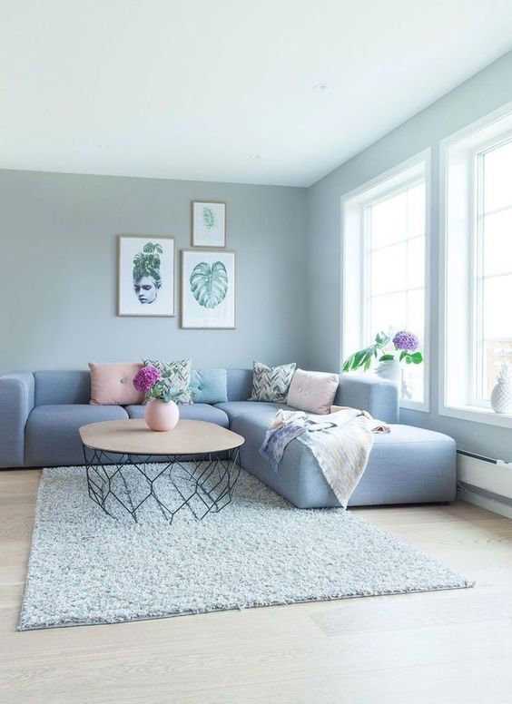 a grey living room with a dusty blue low sofa, printed and pastel pillows, a coffee table and a grey rug is a lovely space