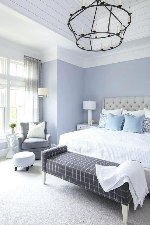 a lilac bedroom with a grey upholstered bed, neutral bedding, a windowpane upholstered bench, a grey chair and a vintage chandelier