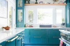 a lovely bright blue kitchen with shaker and glass front cabinets, white countertops, gold handles and a bold printed rug is wow