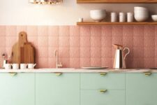 a lovely mint green kitchen with flat panel cabinets, a pink patterned tile backsplash, open shelves and a rose gold pendant lamp