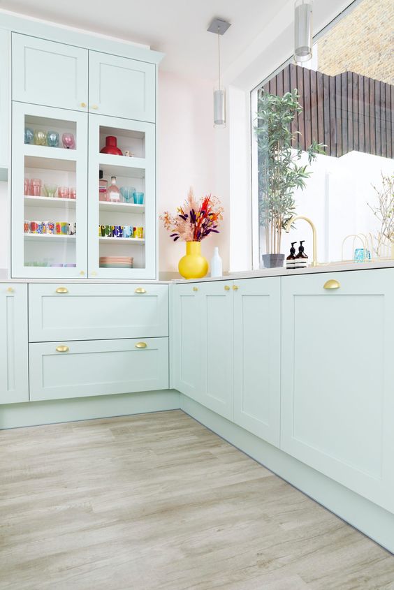 a lovely mint green kitchen with shaker cabinets and glass front ones, gold handles and neutral countertops is amazing