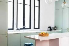 a lovely pastel kitchen with pastel green cabinets and a pink kitchen island, black and white tiles and black stools