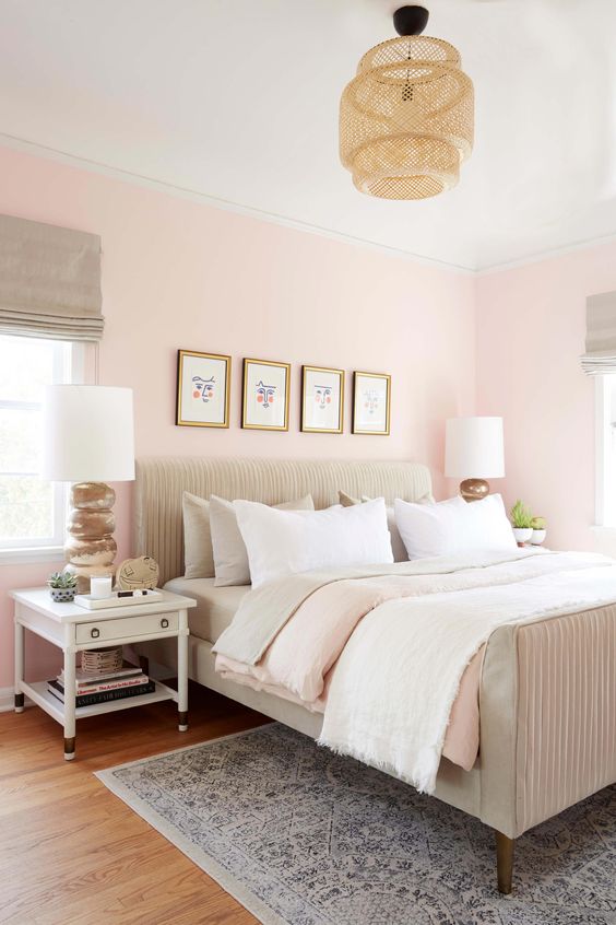 a lovely pastel pink bedroom with a neutral upholstered bed, neutral bedding, white nightstands, neutral curtains and table lamps