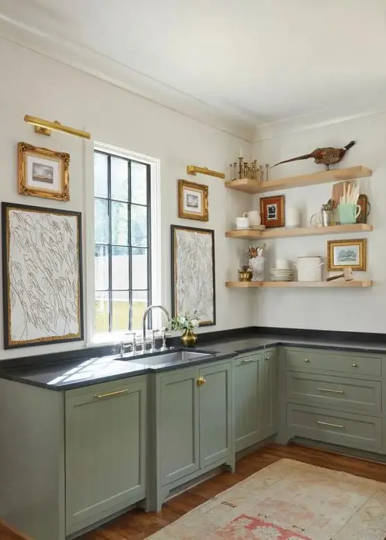 a lovely sage green kitchen with shaker cabinets with black countertpos, open shelves, vintage artwork is pure elegance