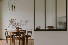 a mid-century modern dining room with a fluted glass partition and a stained table and chairs, pendant lamps and some dried branches
