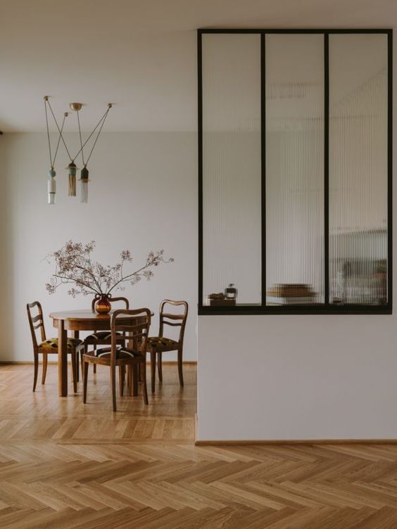 a mid-century modern dining room with a fluted glass partition and a stained table and chairs, pendant lamps and some dried branches