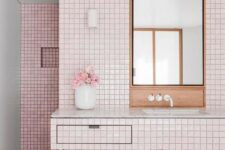 a millenial pink bathroom with a floating vanity clad with tiles, stained wood and black grout to make a contrast