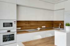 a minimalist kitchen with sleek white cabinets, a wooden backsplash and countertops, a kitchen island that doubles as a table