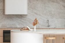 a minimalist kitchen with stained lower cabinets, a large hood, a curved kitchen island, tall stools and a grey marble backsplash