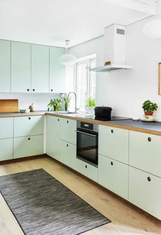 a mint green Scandinavian kitchen with MDF cabinets, black countertops and a white backsplash, a dark rug and built in appliances