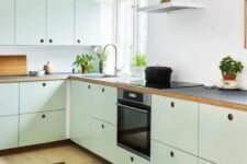 a mint green kitchen with plywood cabinets, a white backsplash, black countertops, no handles and built-in appliances