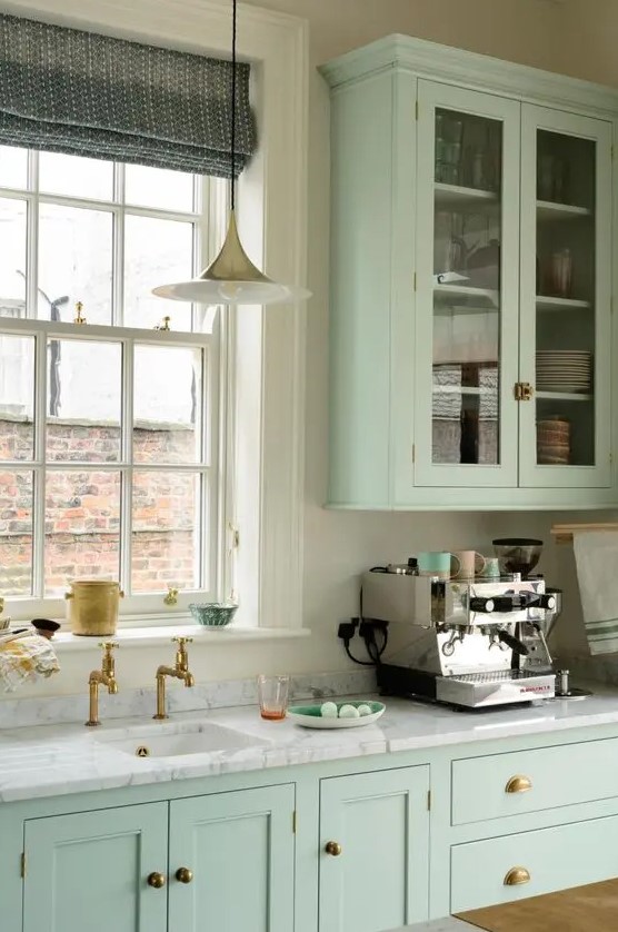 a mint green kitchen with shaker, flat and glass front cabinets, a white quartz countertop and a cool pendant lamp