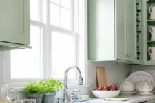 a mint green kitchen with white stone countertops and a white tile backsplash, stainless steel appliances and woven touches