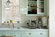a mint green kitchen with white stone countertops, brass handles, a window to brign some natural light in